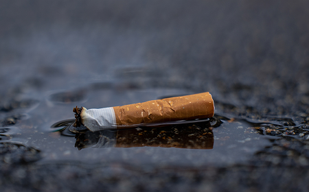 Окурок сигареты в луже на мокром асфальте